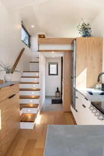 A staircase with white oak treads accesses the loft-style bedroom. The kitchen counters and bathroom flooring are crafted from concrete mixed with glass beads that give the material an organic feel and a lighter weight.