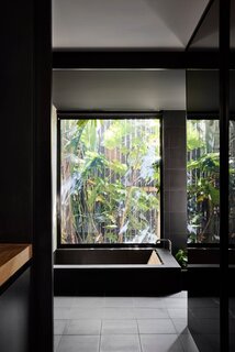 Enormous windows allow light to flood the interior, while carefully framed views of the garden blur the boundaries between interior and exterior. The deep concrete bathtub in the downstairs bathroom, for example, offers views of both internal and external gardens.