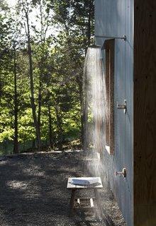 The secluded location of the house at the edge of a retired shale bank allows the luxury of an open outdoor shower. Corrugated steel siding provides a durable, zero-maintenance exterior finish and captures the changing sun and woodland shadows.