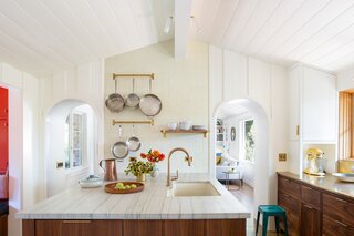 Quartzite kitchen island countertops and a wall of off-white ceramic tile between the doorways complement the space's walnut cabinetry and brass surfaces.